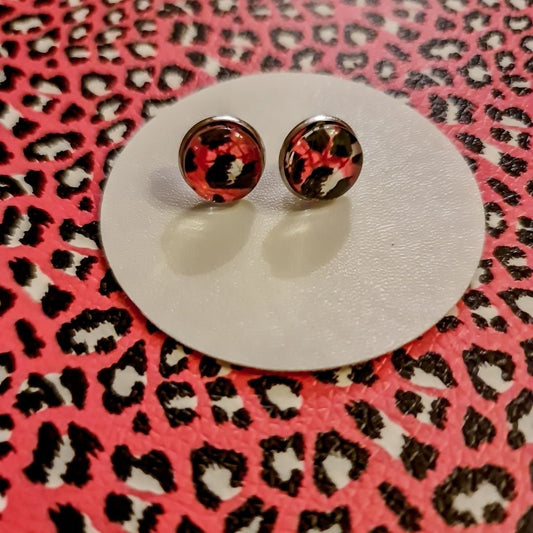 A pair of pink leopard print stud earrings on a pink faux leather background.