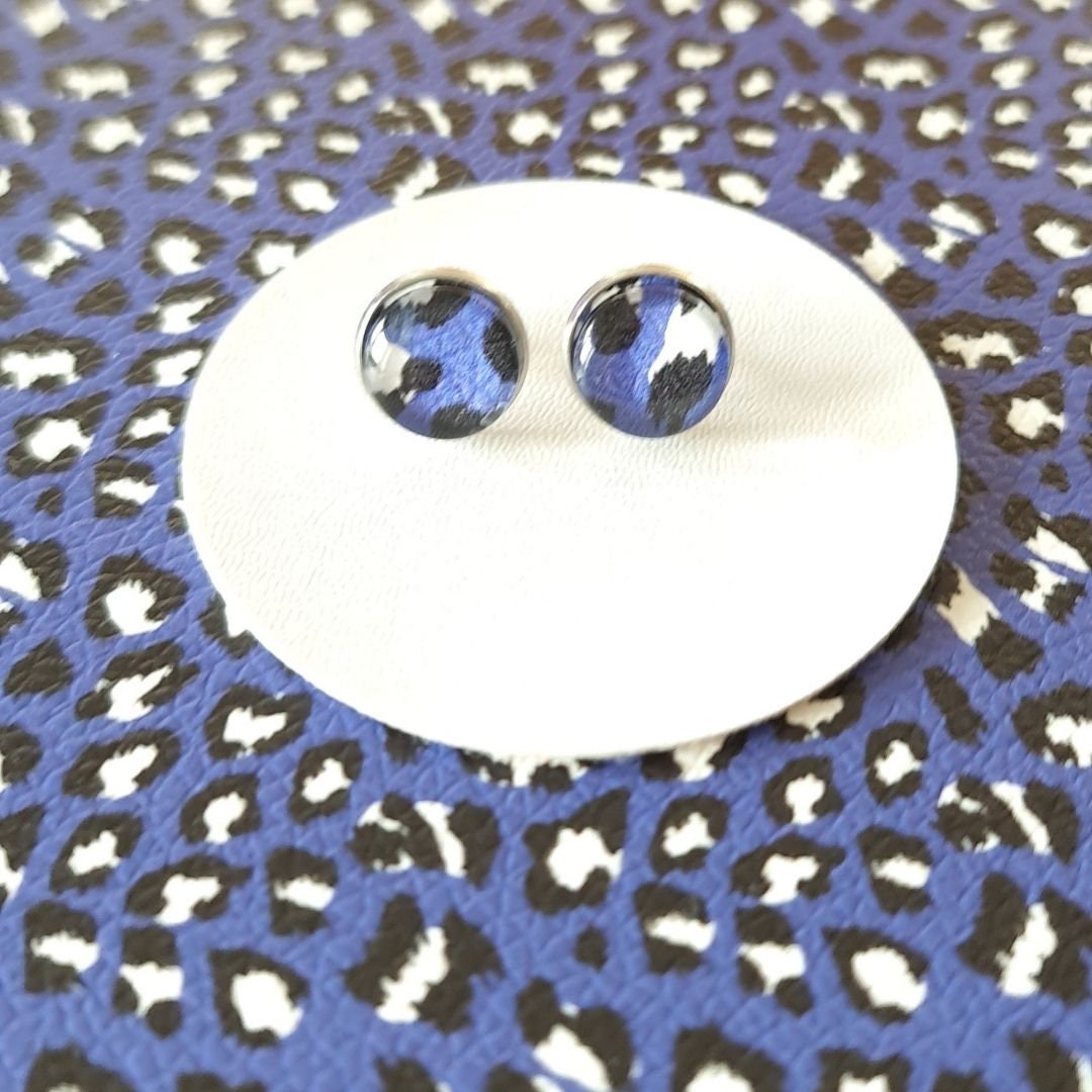 A pair of blue leopard print stud earrings on a faux leather, blue leopard print background.